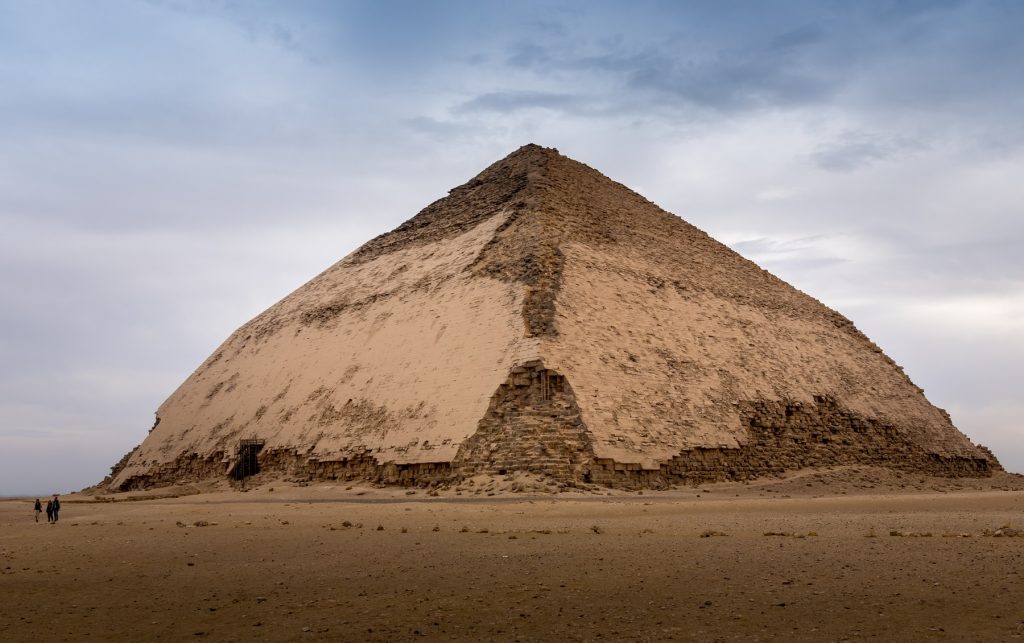 A view of the Bent Pyramid of Sneferu. People standing next to the pyramid. Shutterstock.